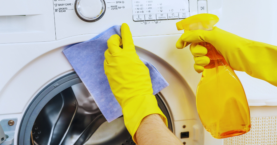 person wearing gloves wiping a washing machine with a cleaner