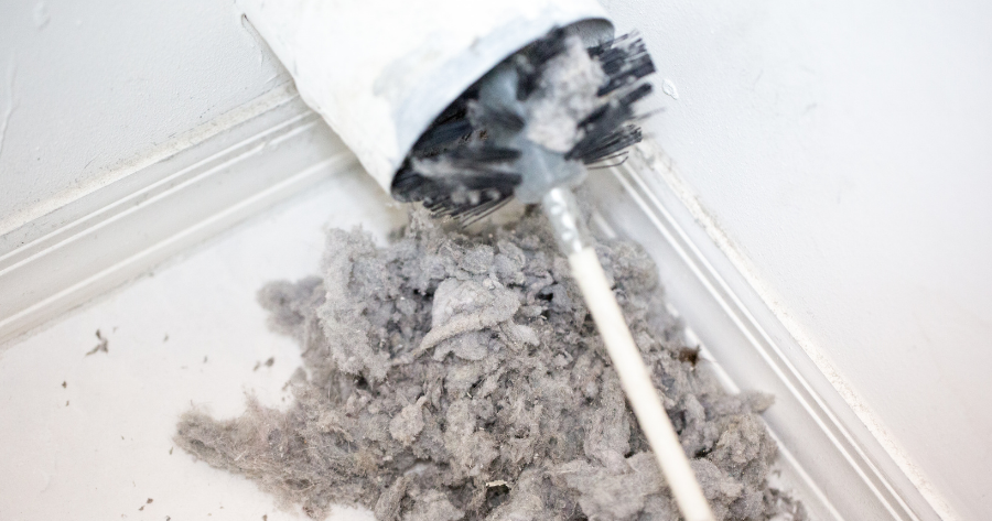 dryer vent being cleaned with a round brush and a pile of lint on the floor