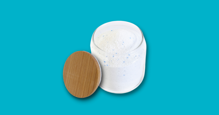 powder laundry detergent in a glass jar with bamboo lid against blue background